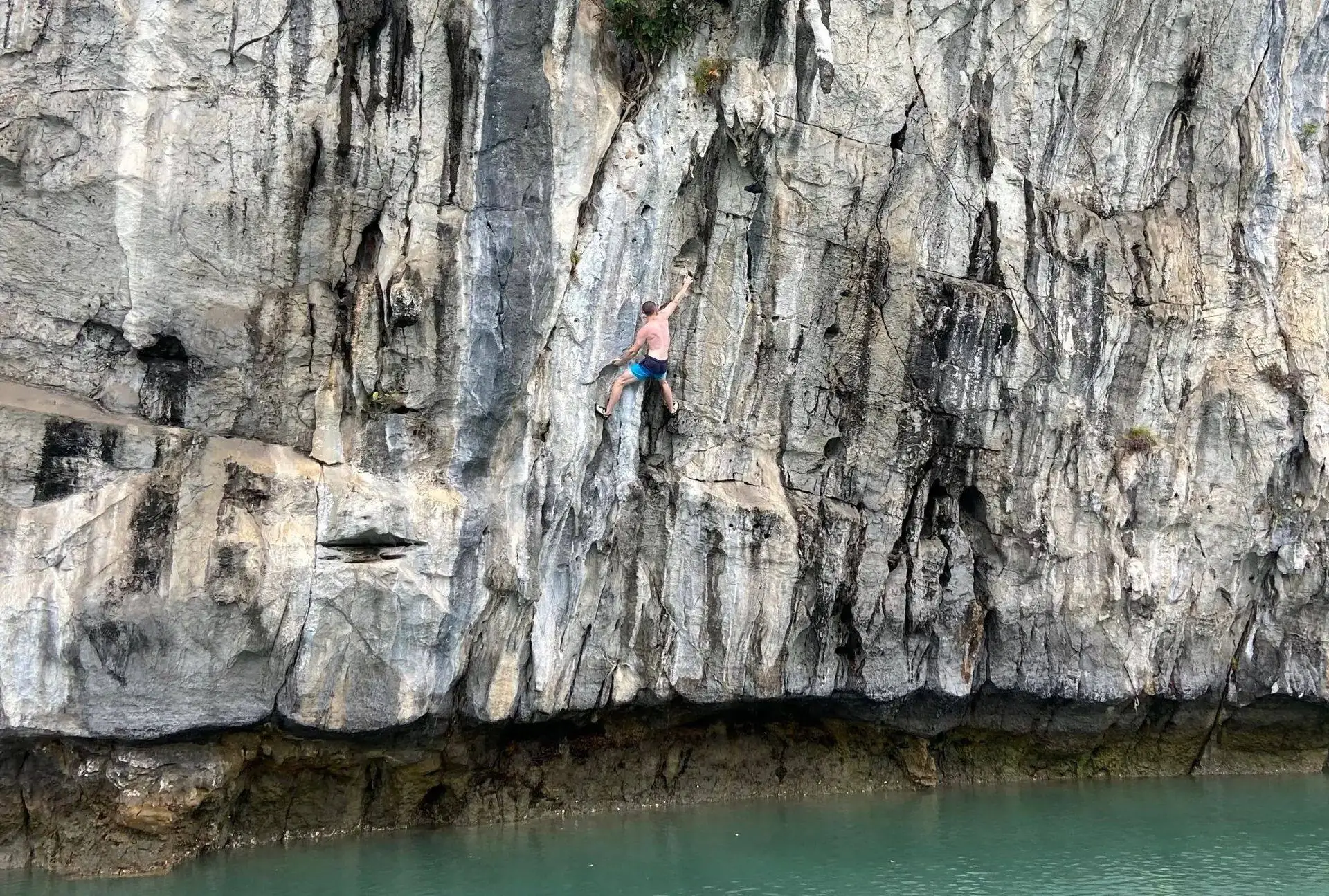 Grimpeur en Deep Water Solo sur un devers calcaire au-dessus de l'eau turquoise, baie de Lan Ha, Vietnam